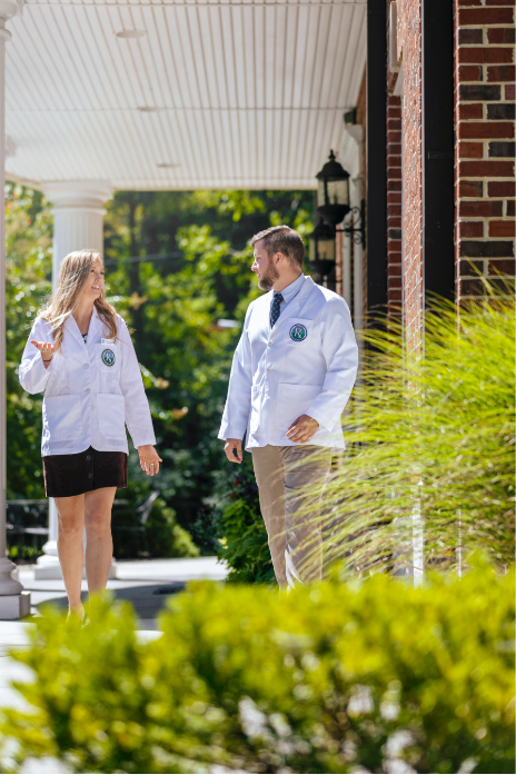two students in lab coats walking on campus