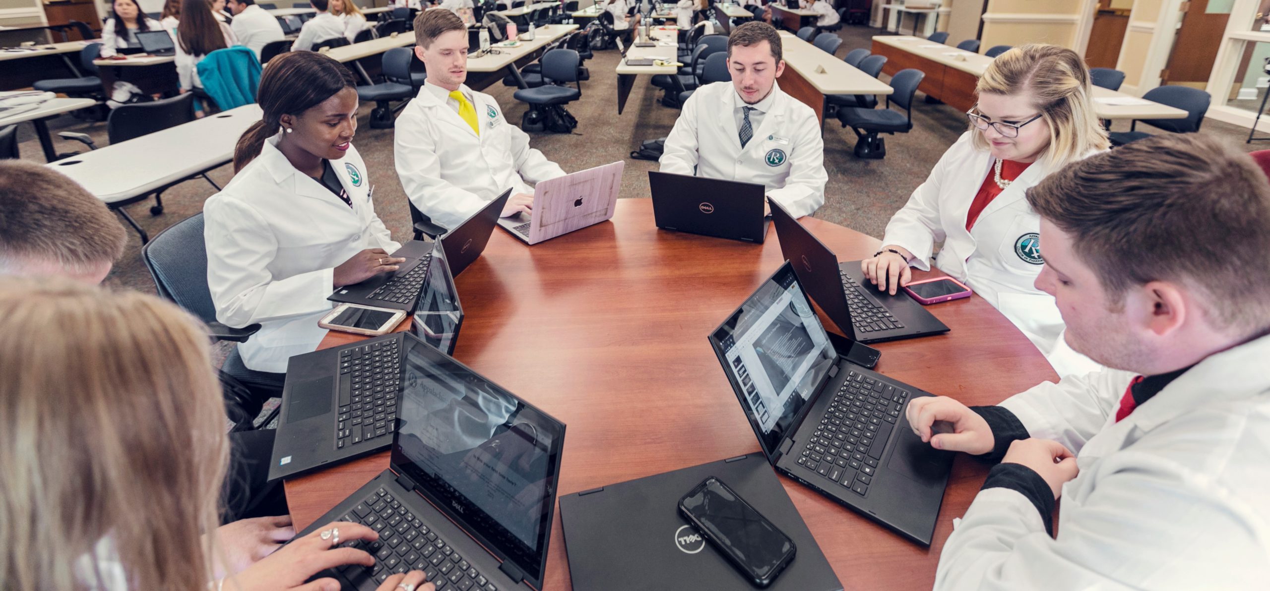 student group in lab coats working on laptops