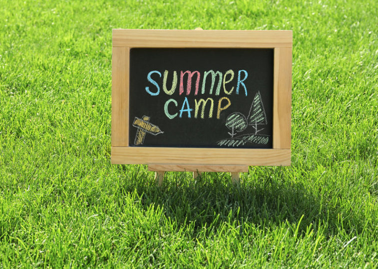 Blackboard with text SUMMER CAMP and drawings on green grass